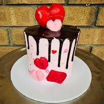 Pink and white chocolate drip cake with red heart decorations and pink fondant hearts